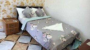Un lit bien fait, avec une literie à motifs floraux, une table de chevet en bois dotée de tiroirs et un sol à motifs.