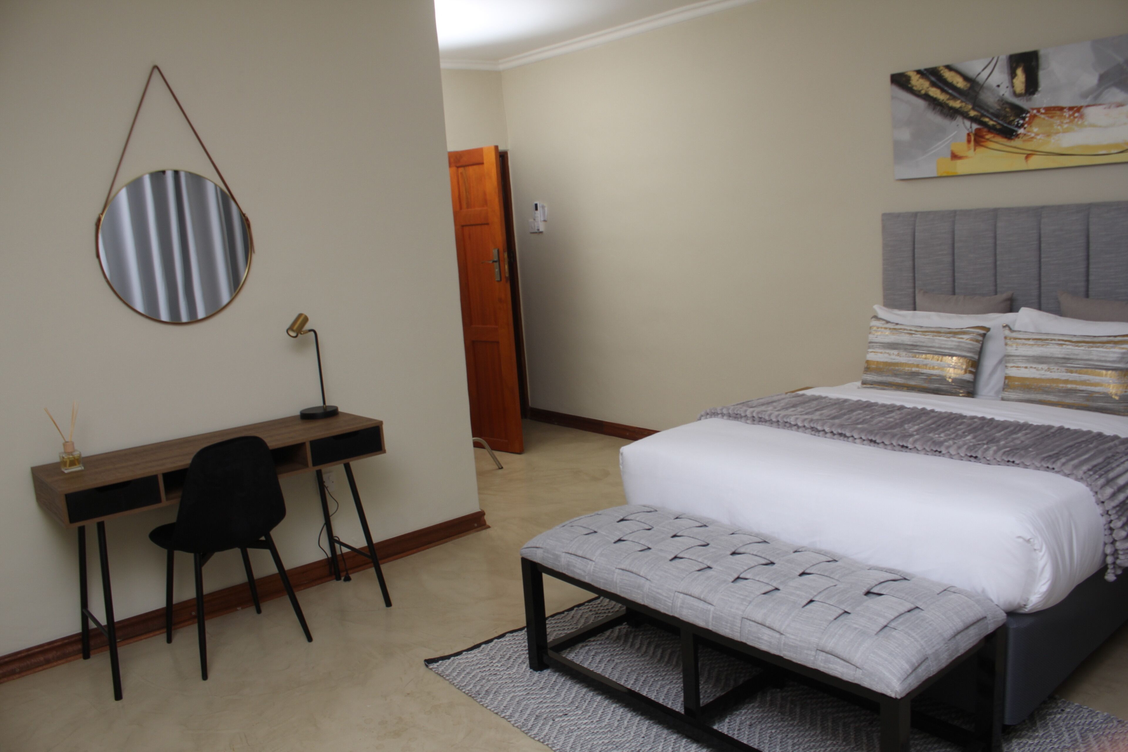 A bedroom with a bed, a desk, a chair, and a mirror.
