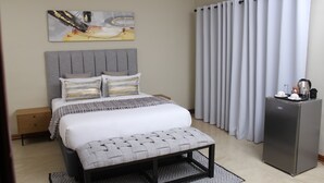A modern bedroom with a bed, a bench, a nightstand, a refrigerator, and a curtain. - The Oak Tree House (Gaborone)