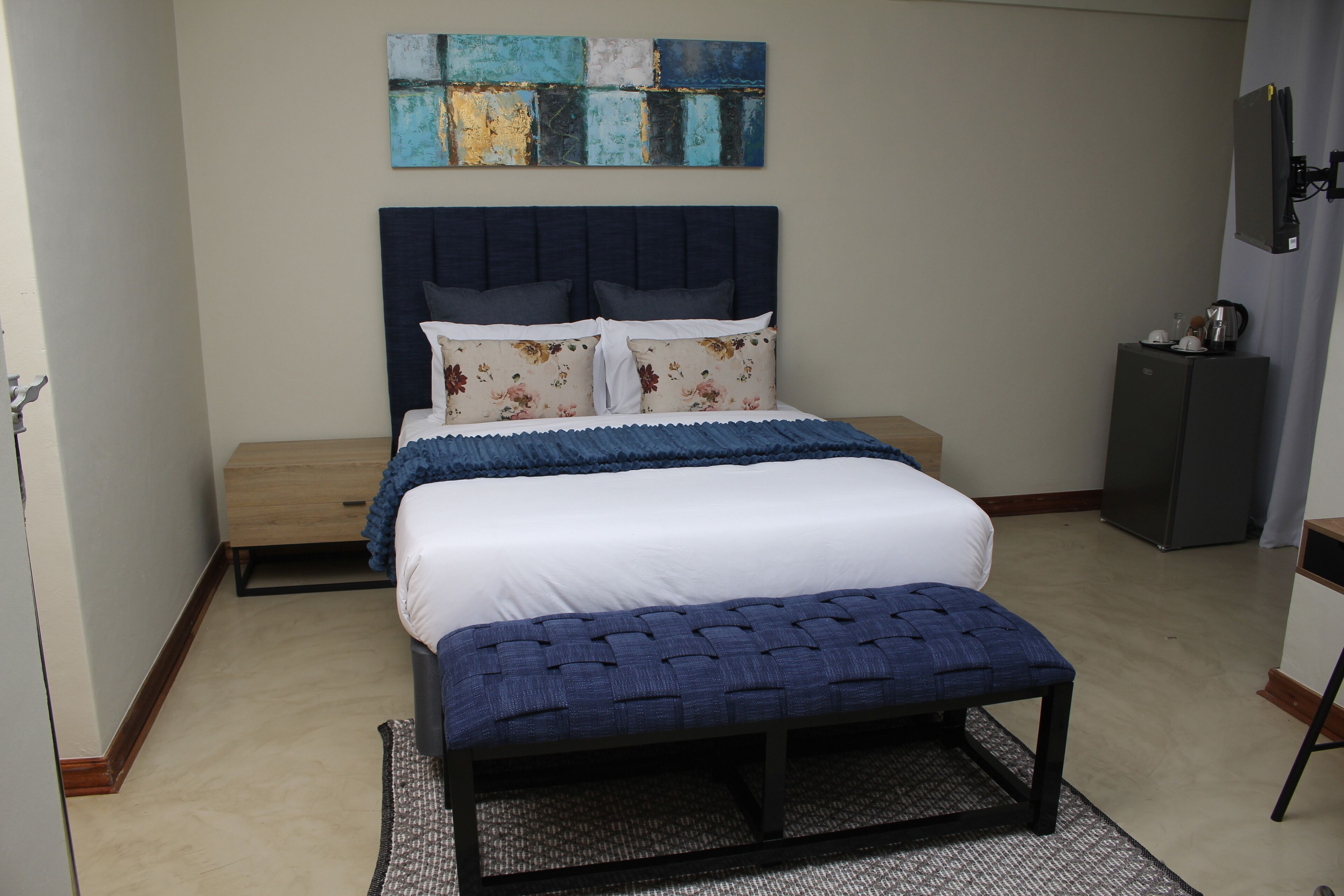 A bedroom with a bed, a bench, a dresser, and a wall-mounted TV.