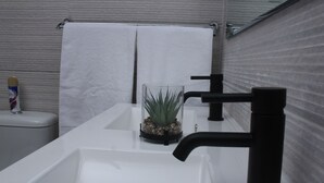 A modern bathroom with a white sink, black faucet, and a small potted plant on the counter. - The Oak Tree House (Gaborone)