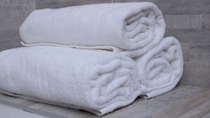 A stack of white towels on a wooden surface with a tiled wall in the background. - The Oak Tree House (Gaborone)