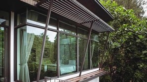 A modern room with large windows, a wooden bench, and a view of greenery outside. - Khaoyai Valley 2 (Pak Chong)