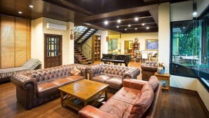 A spacious living room with leather sofas, a wooden coffee table, and a piano. - Khaoyai Valley 2 (Pak Chong)
