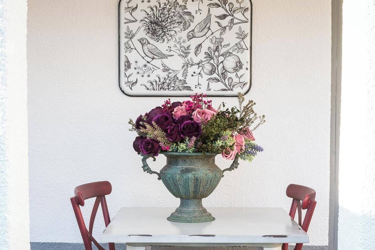 Uma mesa de jantar com um vaso de flores, duas cadeiras vermelhas e uma obra de arte emoldurada na parede.