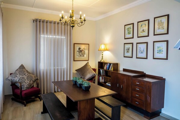 A dining area with a wooden table, bench, chandelier, and a bookshelf with framed pictures.