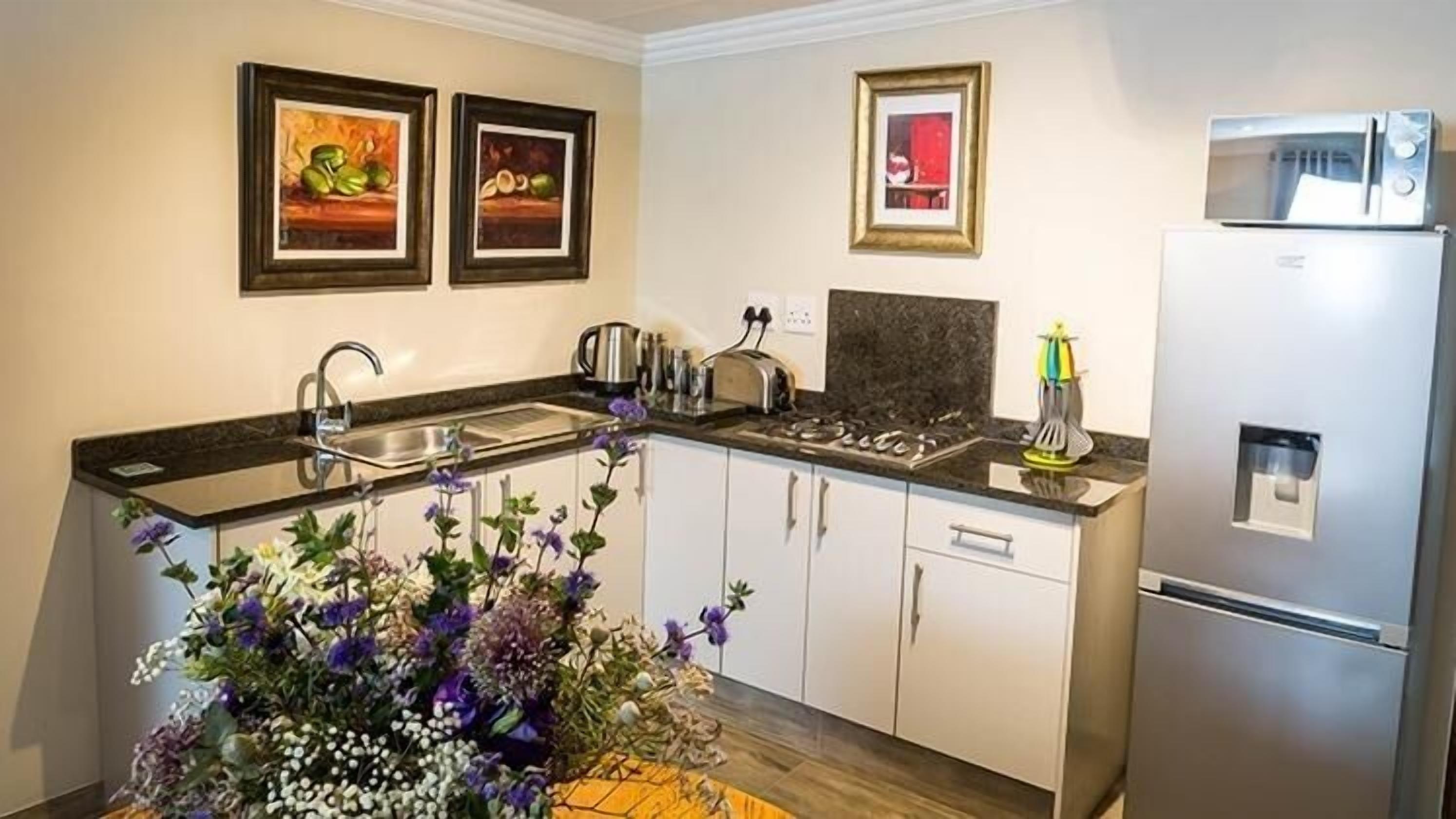 Une cuisine moderne équipée d’un évier, d’une cuisinière et d’un réfrigérateur. Des tableaux encadrés ornent le mur et un arrangement floral est posé sur le plan de travail.