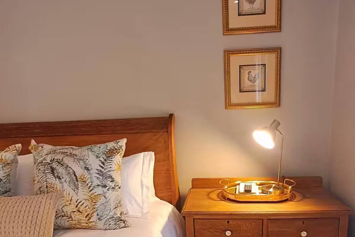 Cama bem arrumada com almofadas florais, luminária de cabeceira e mesa de cabeceira de madeira com bandeja.