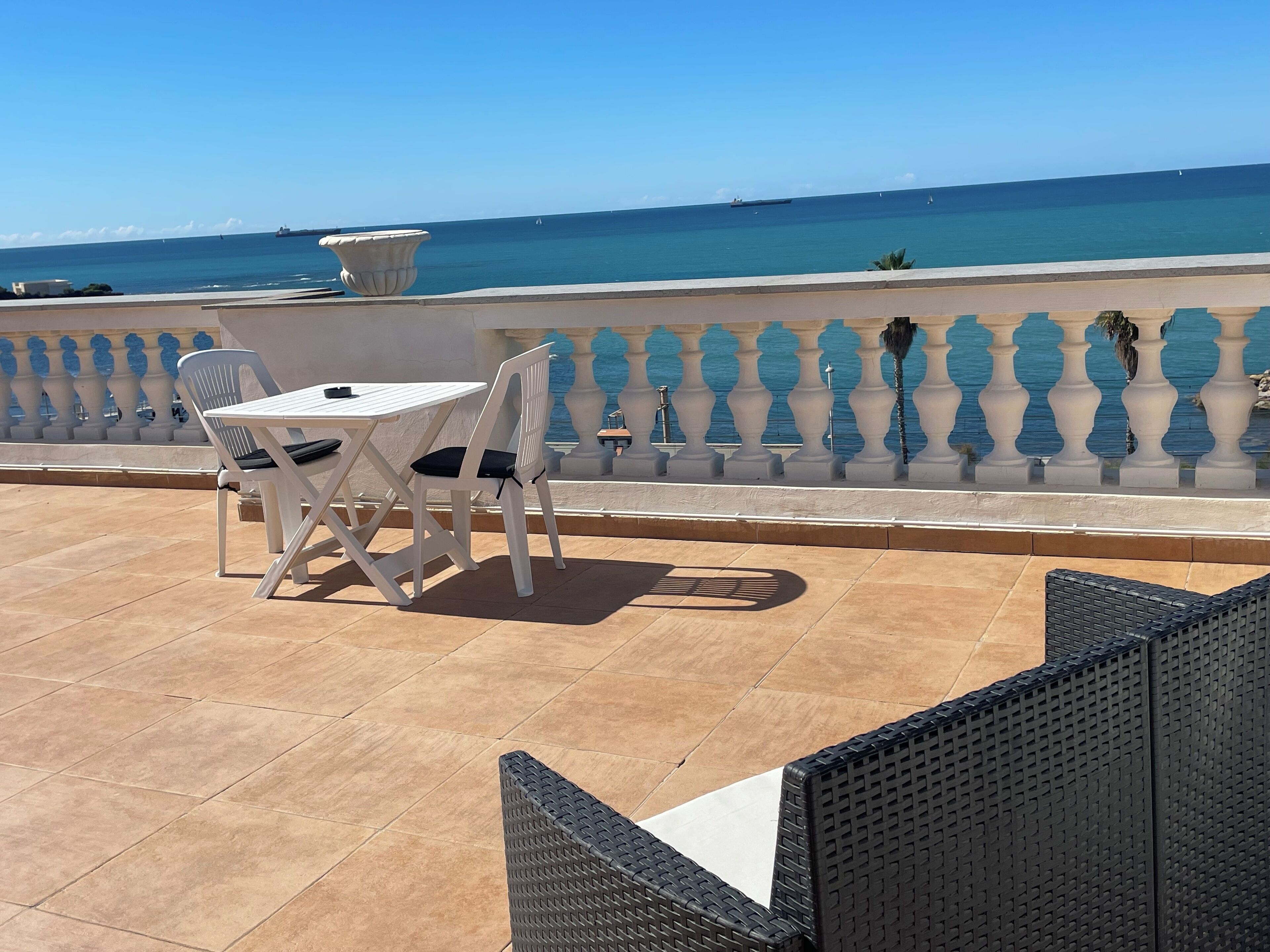 A terrace with a table and chairs, a balustrade, and a view of the sea.