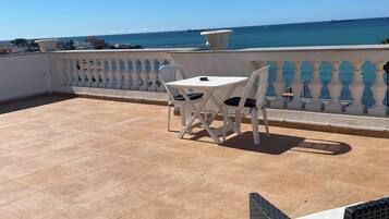 A terrace with a white table and chairs, a view of the sea, and a balustrade.