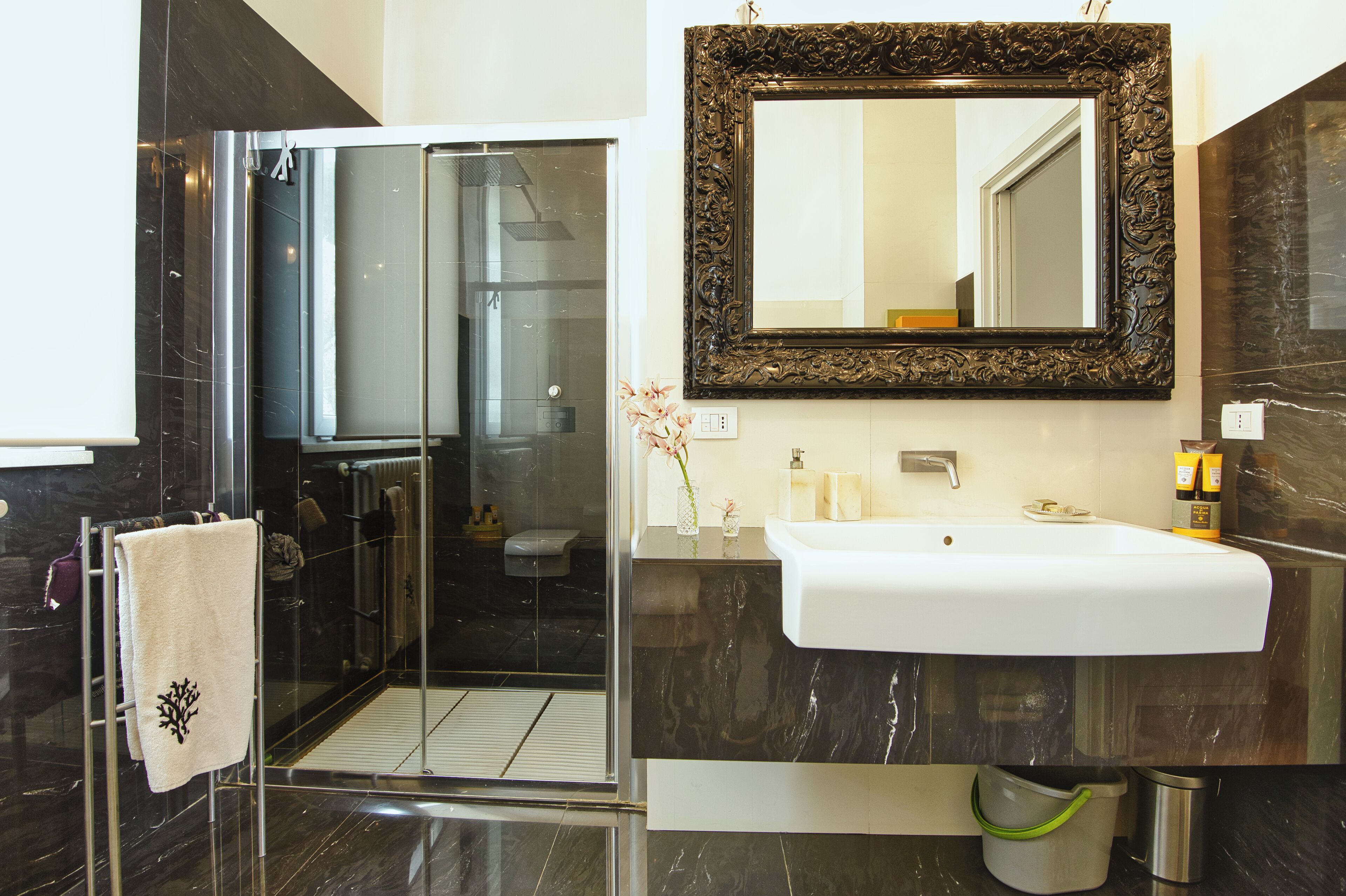 A modern bathroom with a glass shower enclosure, a white sink, and a large ornate mirror.