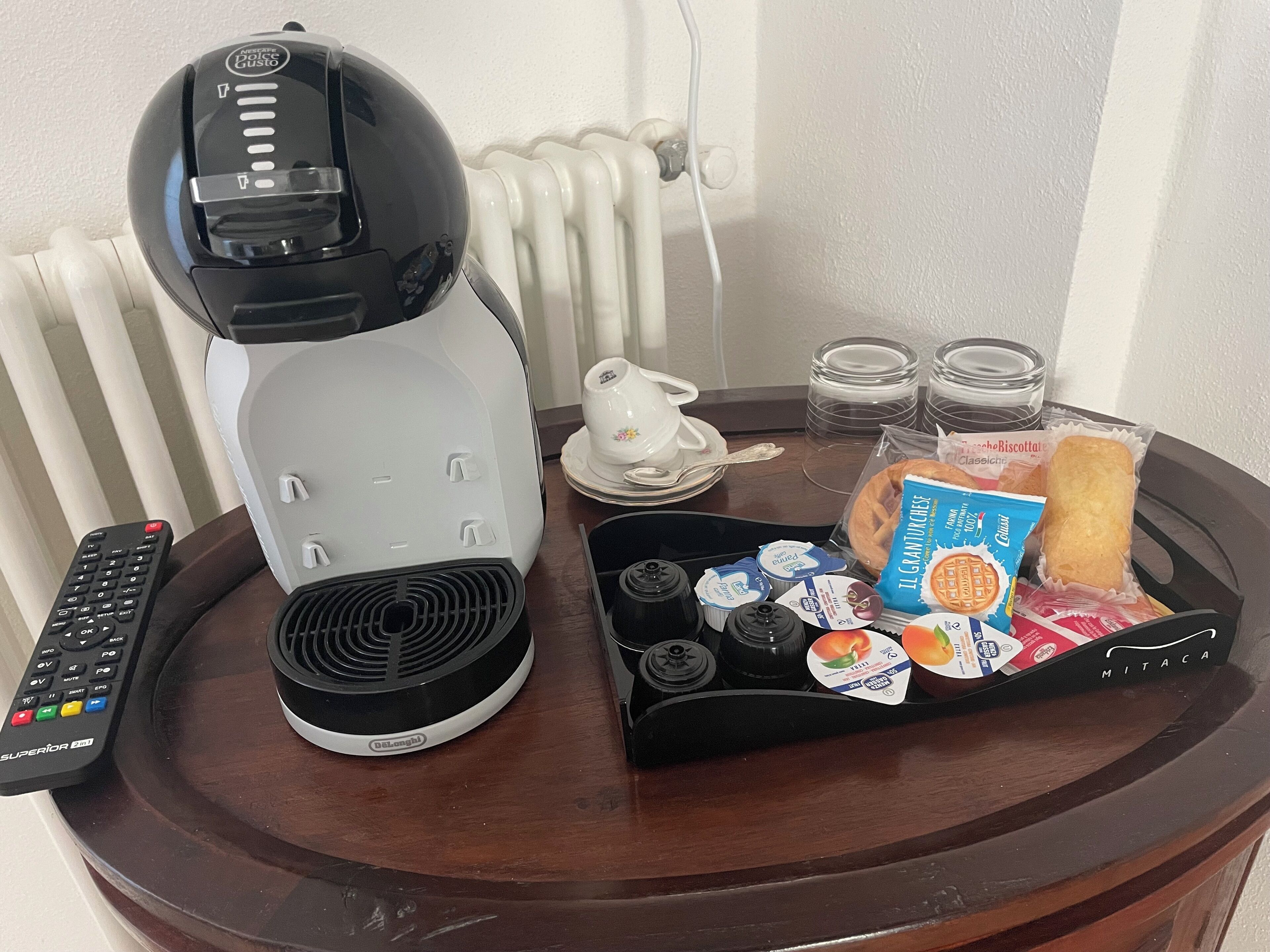 Una cafetera, un control remoto, una bandeja con comida y un hervidor sobre una mesa de madera.