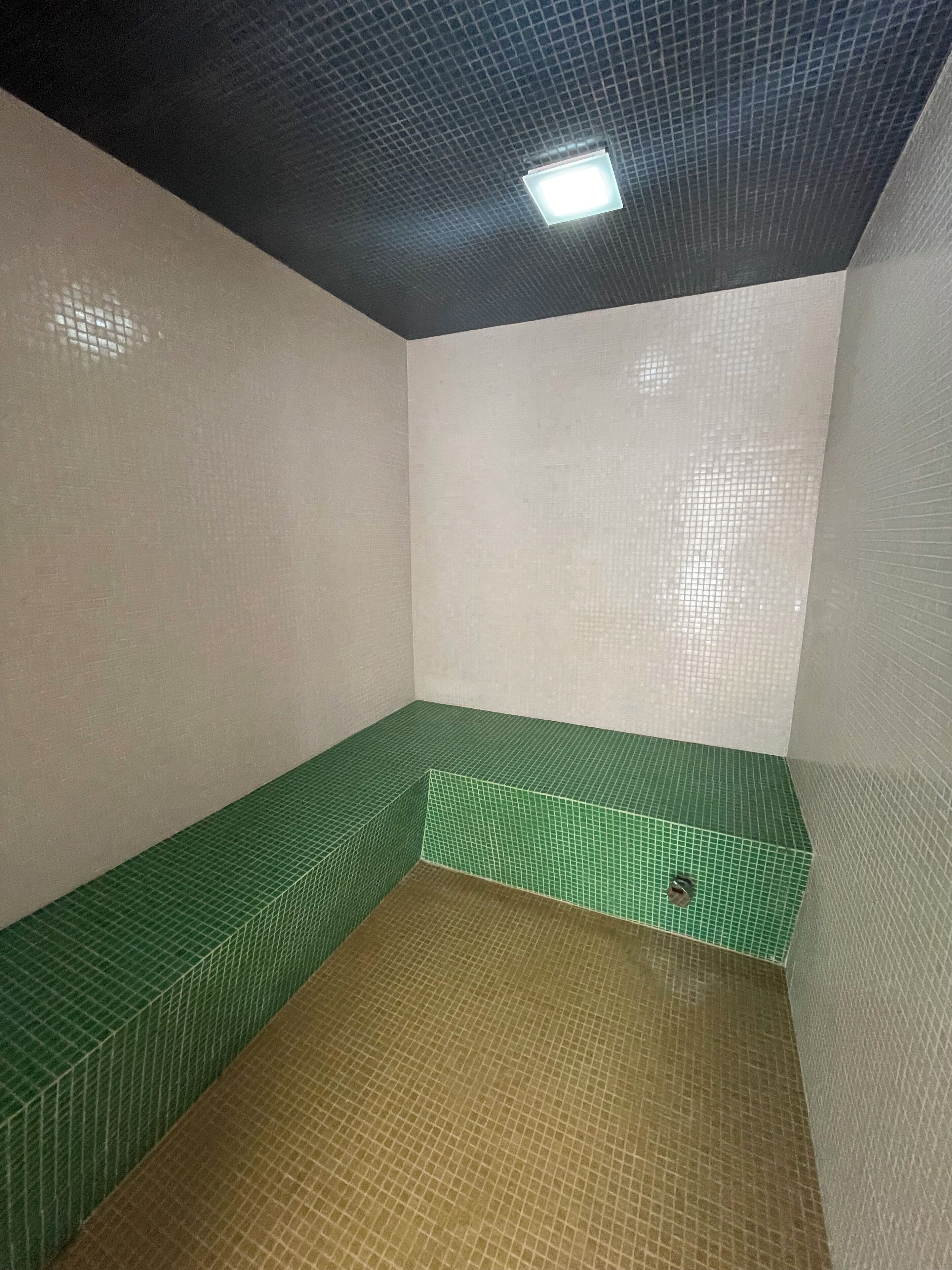 A small, enclosed room with a green-tiled bench and a brown-tiled floor.
