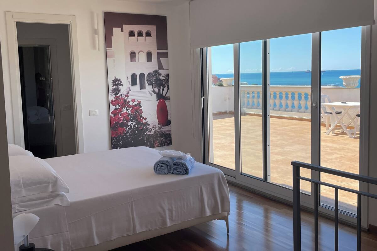Une chambre à coucher avec un lit, une grande fenêtre et un balcon donnant sur la mer.