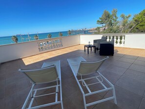 A terrace with two white lounge chairs, a small table, and a view of the sea and buildings in the background. - Palazzo Podestà (Civitavecchia)
