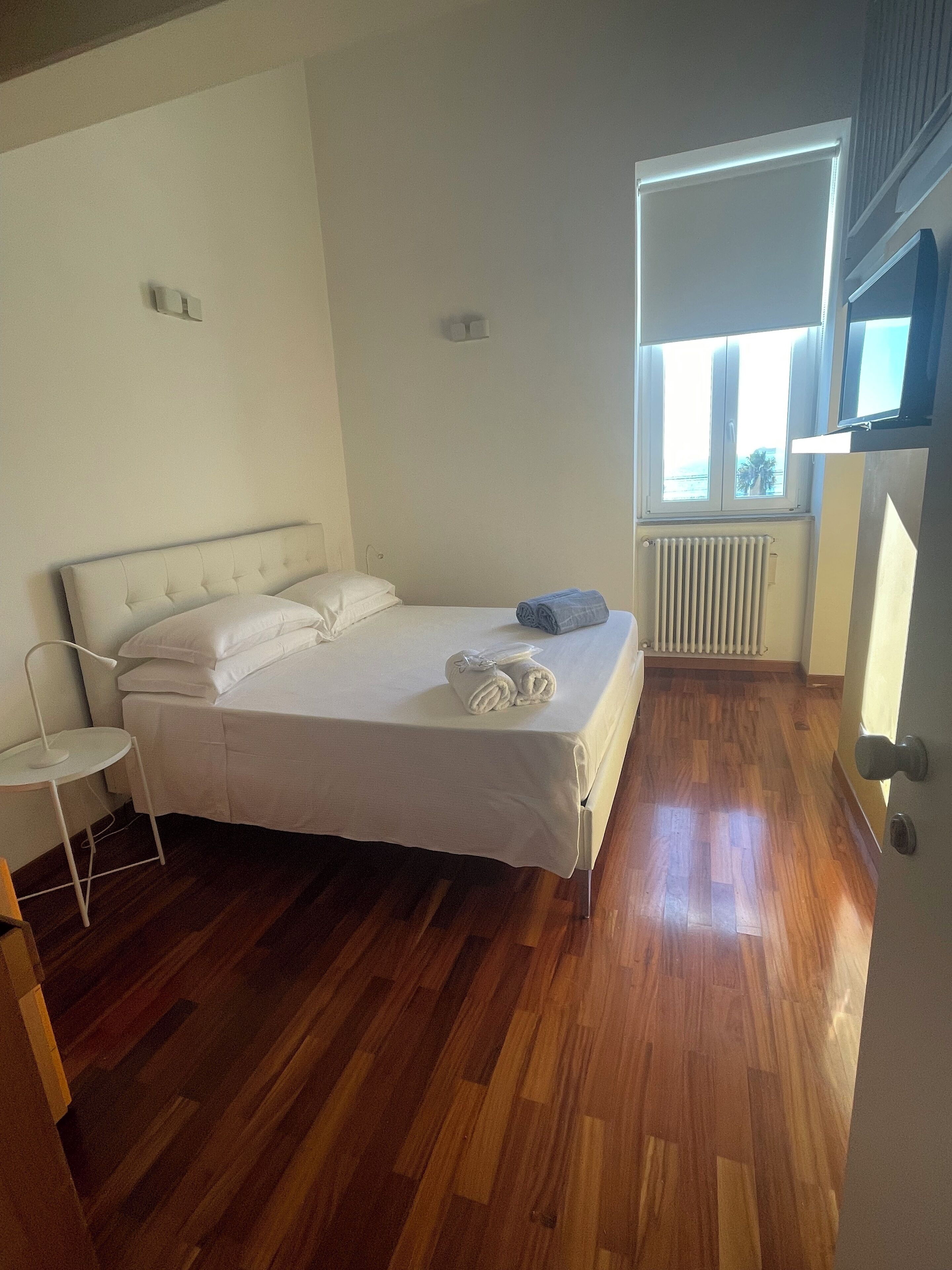 Ein Schlafzimmer mit einem großen Bett, einem Nachttisch, einem Heizkörper und einem Fenster mit Blick.