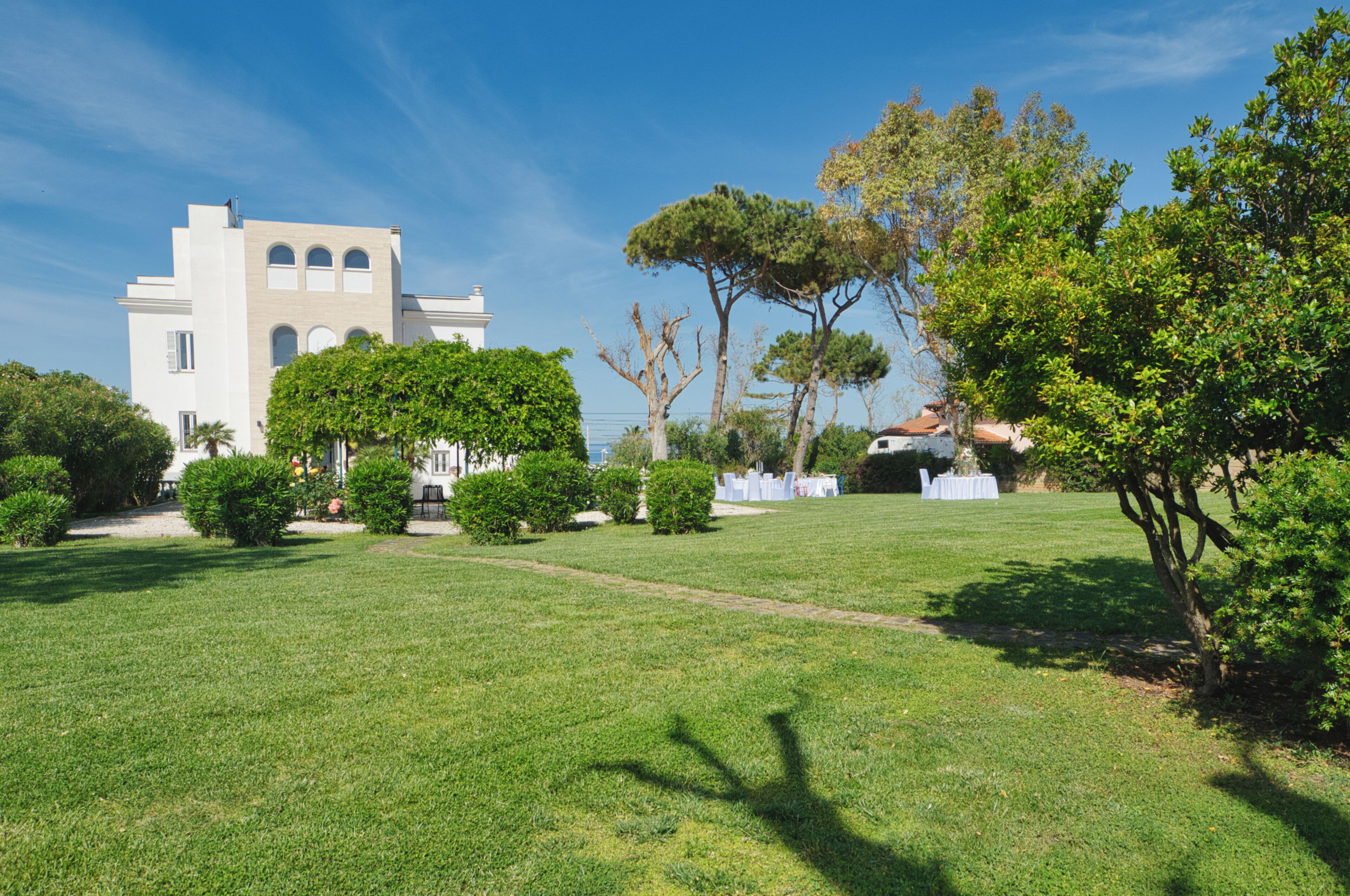 A well-maintained grassy lawn with a white building featuring arched windows and a flat roof.