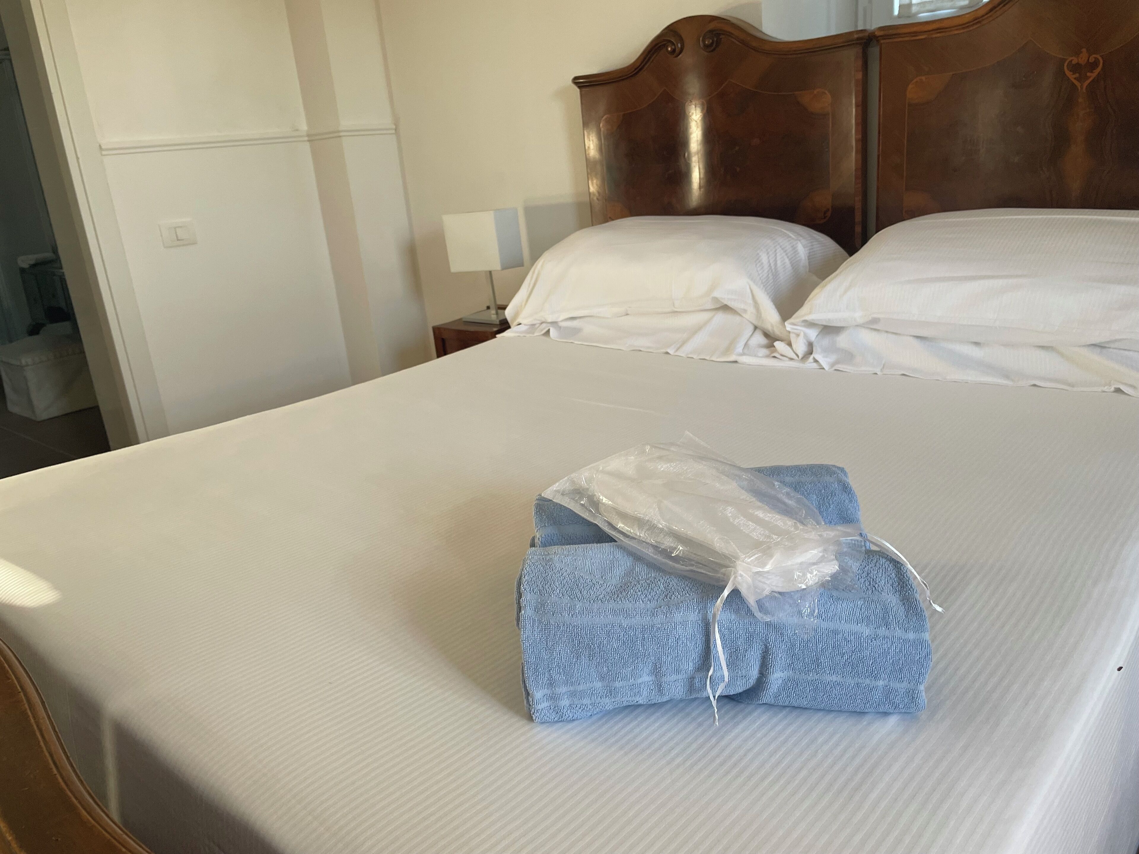 Een net opgemaakt bed met witte lakens, een houten hoofdbord en een blauwe handdoek die op het bed is gevouwen.