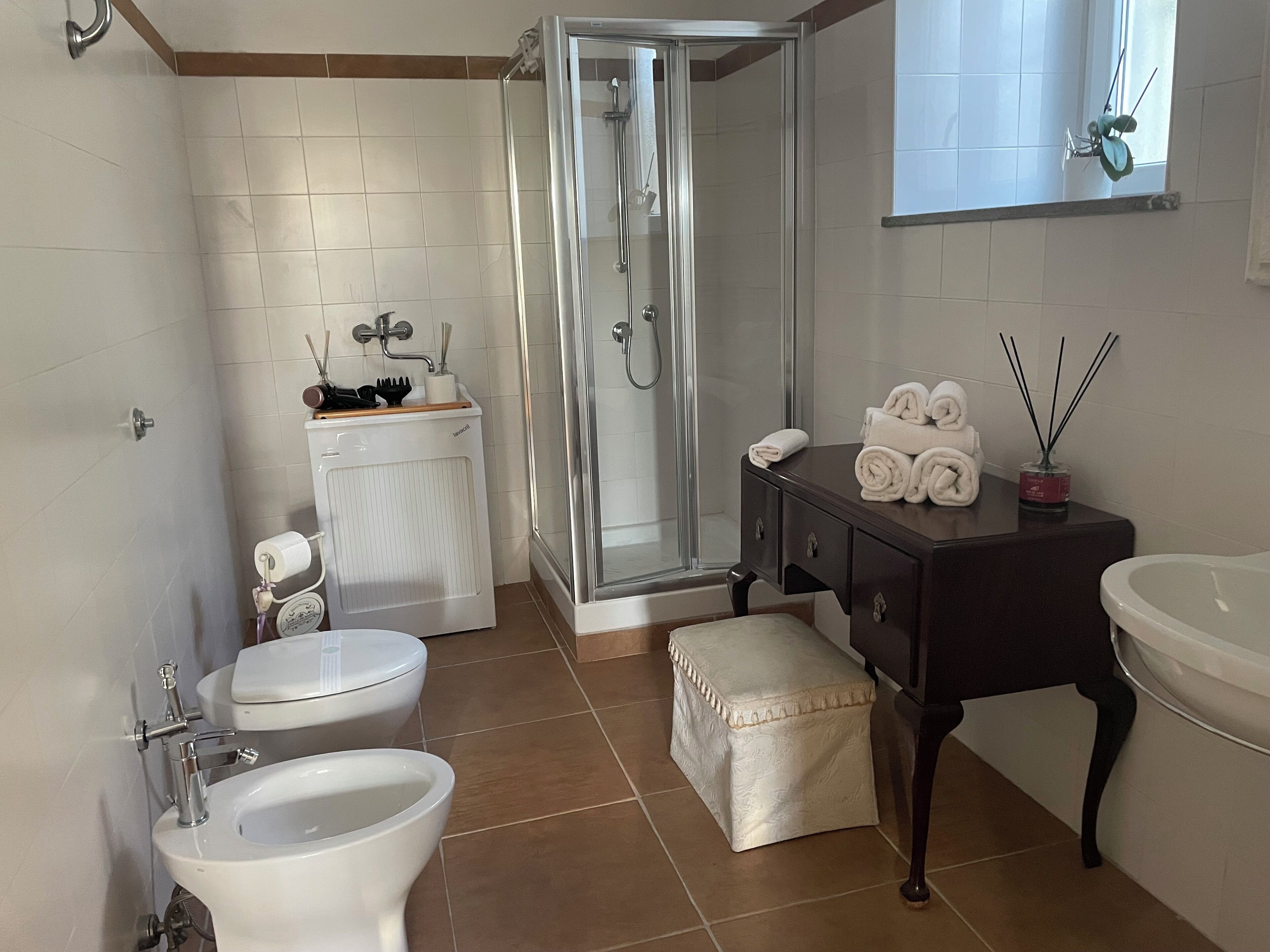 Un baño con ducha de vidrio, dos inodoros, un bidé, un lavabo con espejo y un lavamanos.