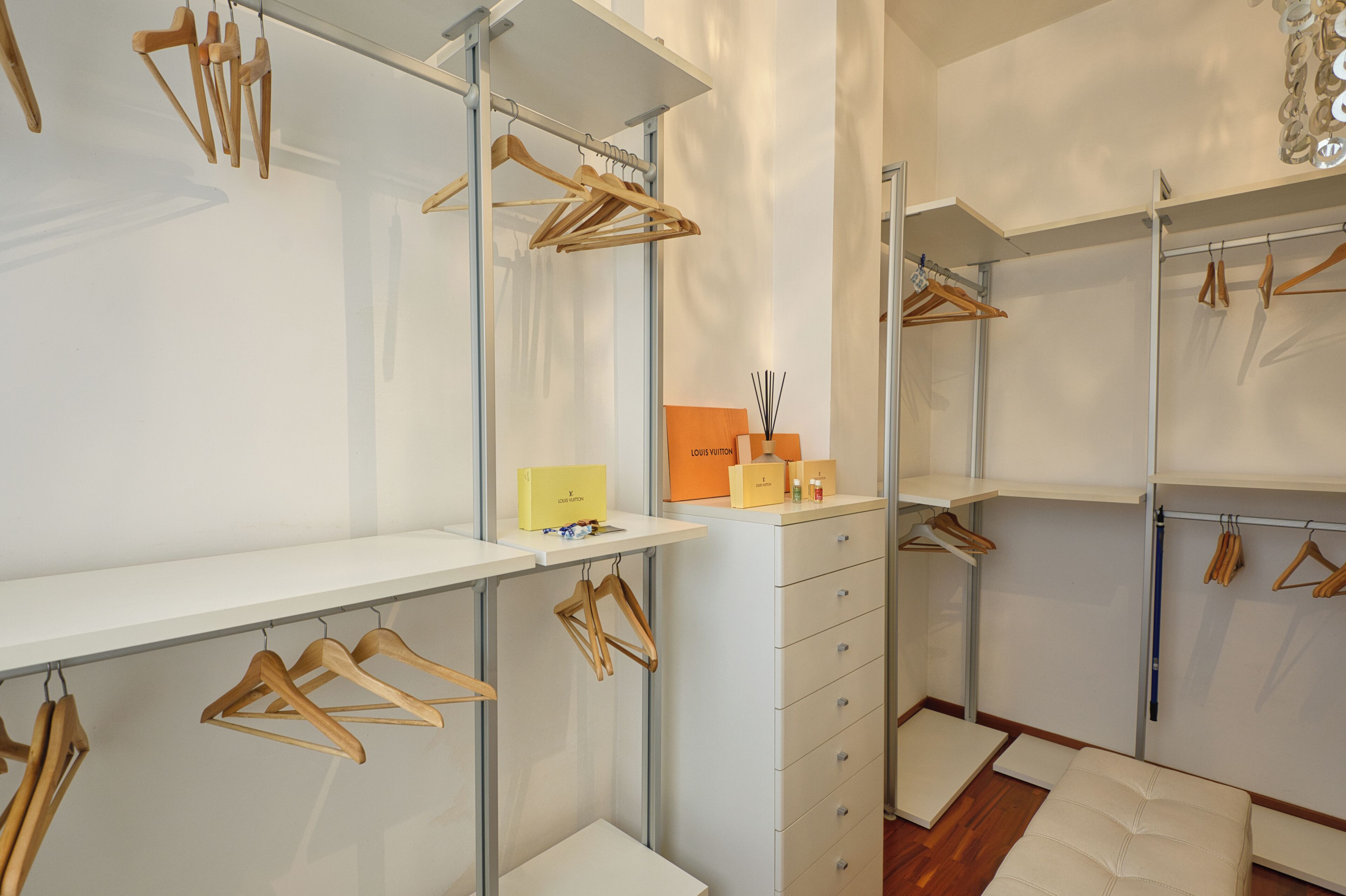 Un placard moderne avec des cintres en bois, une boîte Louis Vuitton et un design minimaliste.