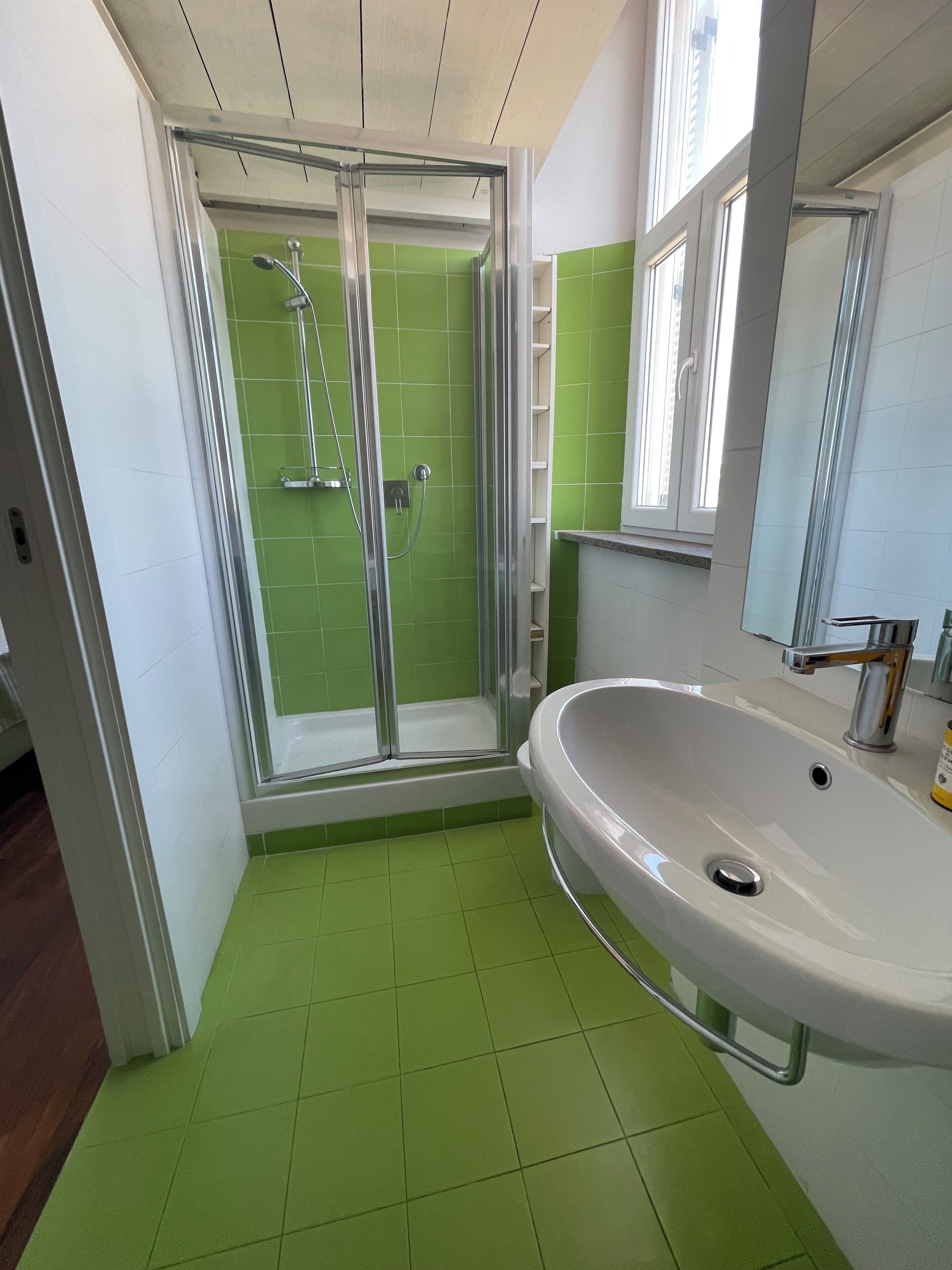 Une salle de bain avec une douche à parois de verre, un lavabo blanc et des murs recouverts de carreaux verts.