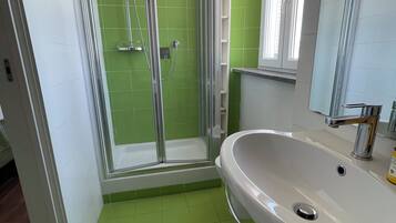 Une salle de bain avec une douche à parois de verre, un lavabo blanc et des murs recouverts de carreaux verts.