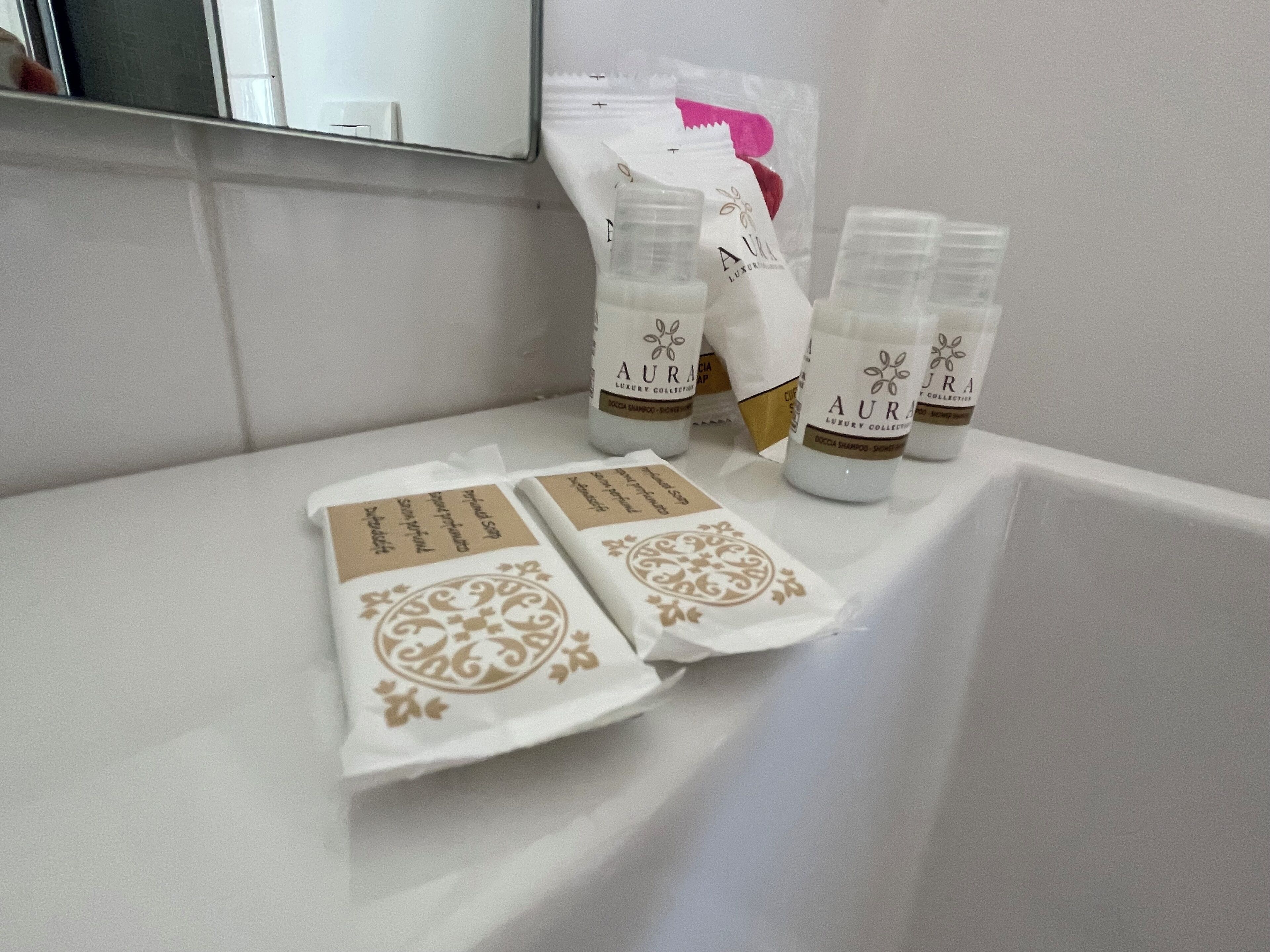 A bathroom with a white sink, a mirror, and toiletries including bottles and packaged items.