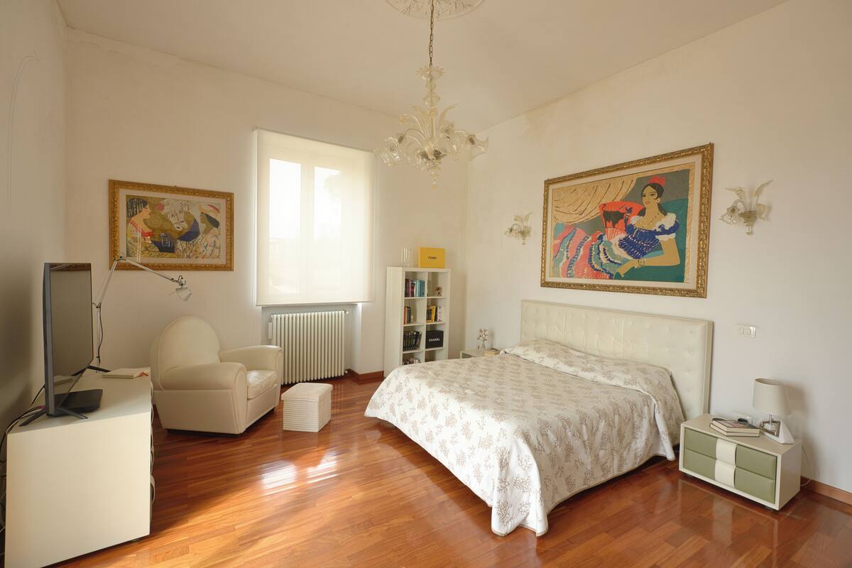Une chambre à coucher comprenant un lit, une chaise, un bureau, un radiateur, une bibliothèque et un tableau accroché au mur.