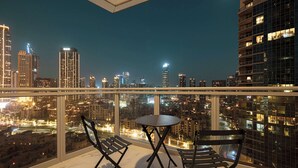 A balcony with a table and two chairs, overlooking a cityscape at night.