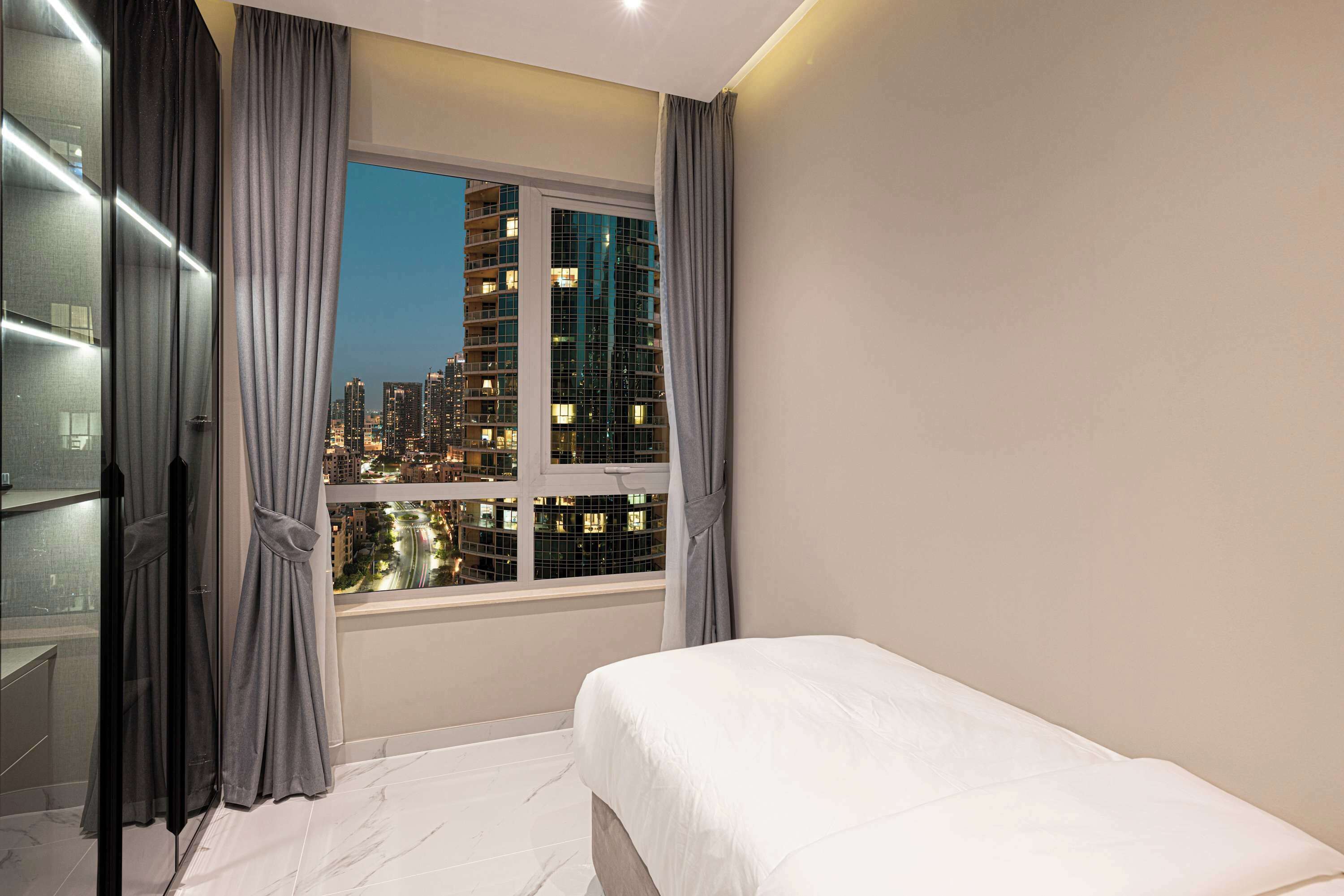Une chambre d’hôtel avec un lit, une fenêtre avec des rideaux et une vue sur le paysage urbain la nuit.