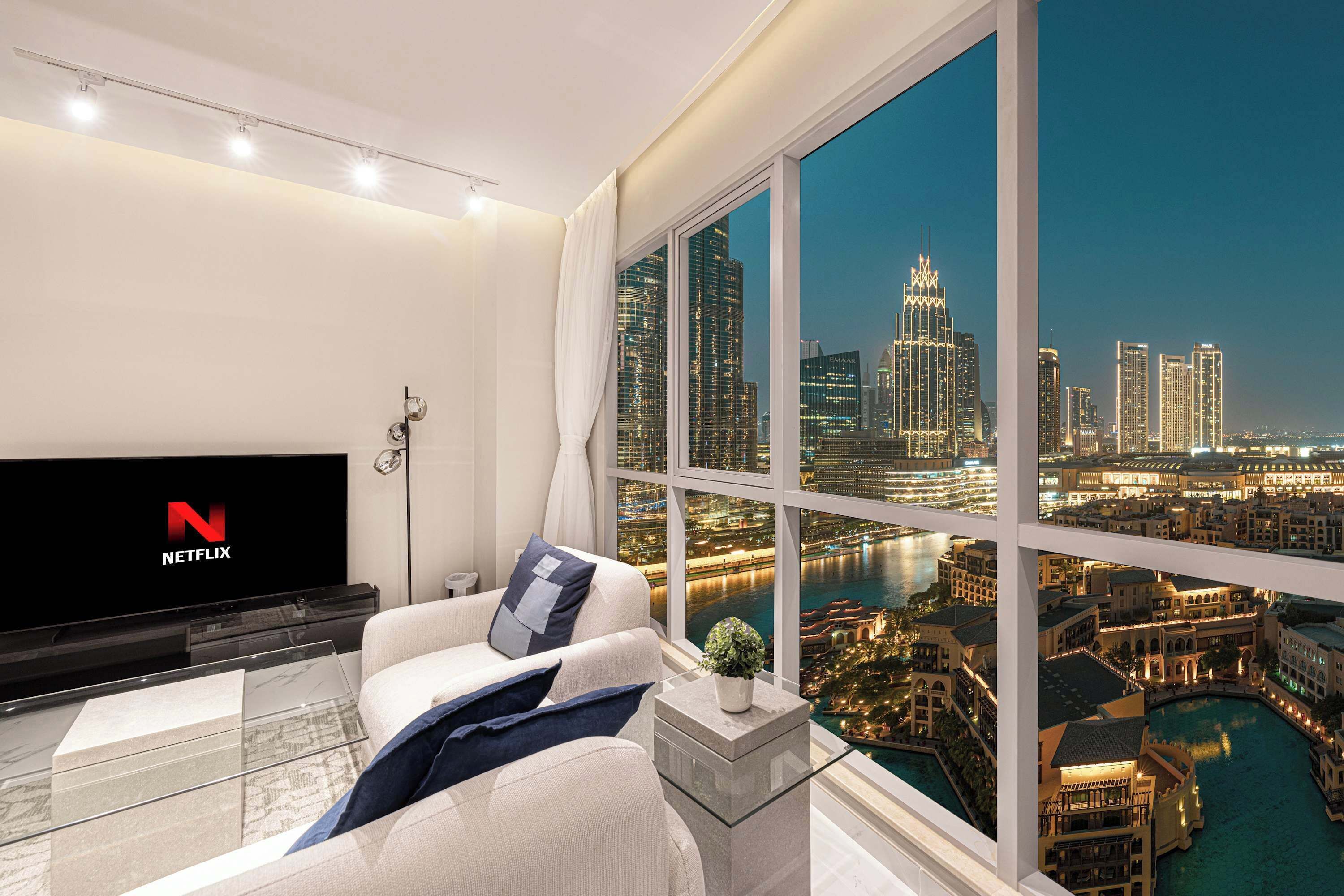 A modern living room with a large window offering a cityscape view, a flat-screen TV, and a glass coffee table.