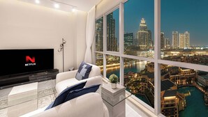 A modern living room with a large window offering a cityscape view, a flat-screen TV, and a glass coffee table.