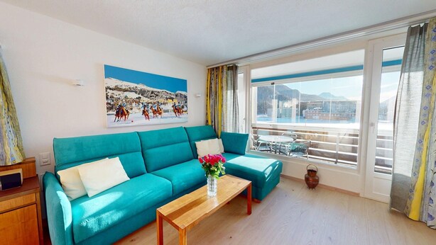 A teal sofa, a wooden coffee table with a vase of flowers, and a painting of a snowy landscape. - Well-kept holiday apartament house in a prime location in St. (St. Moritz)