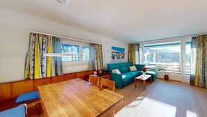 A modern living room with a wooden dining table, teal sofa, and large windows offering city views. - Well-kept holiday apartament house in a prime location in St. (St. Moritz)