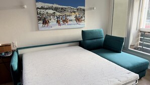A bedroom with a bed, a teal sofa, a painting of a snowy mountain scene, and a window with a view of the outside. - Well-kept holiday apartament house in a prime location in St. (St. Moritz)