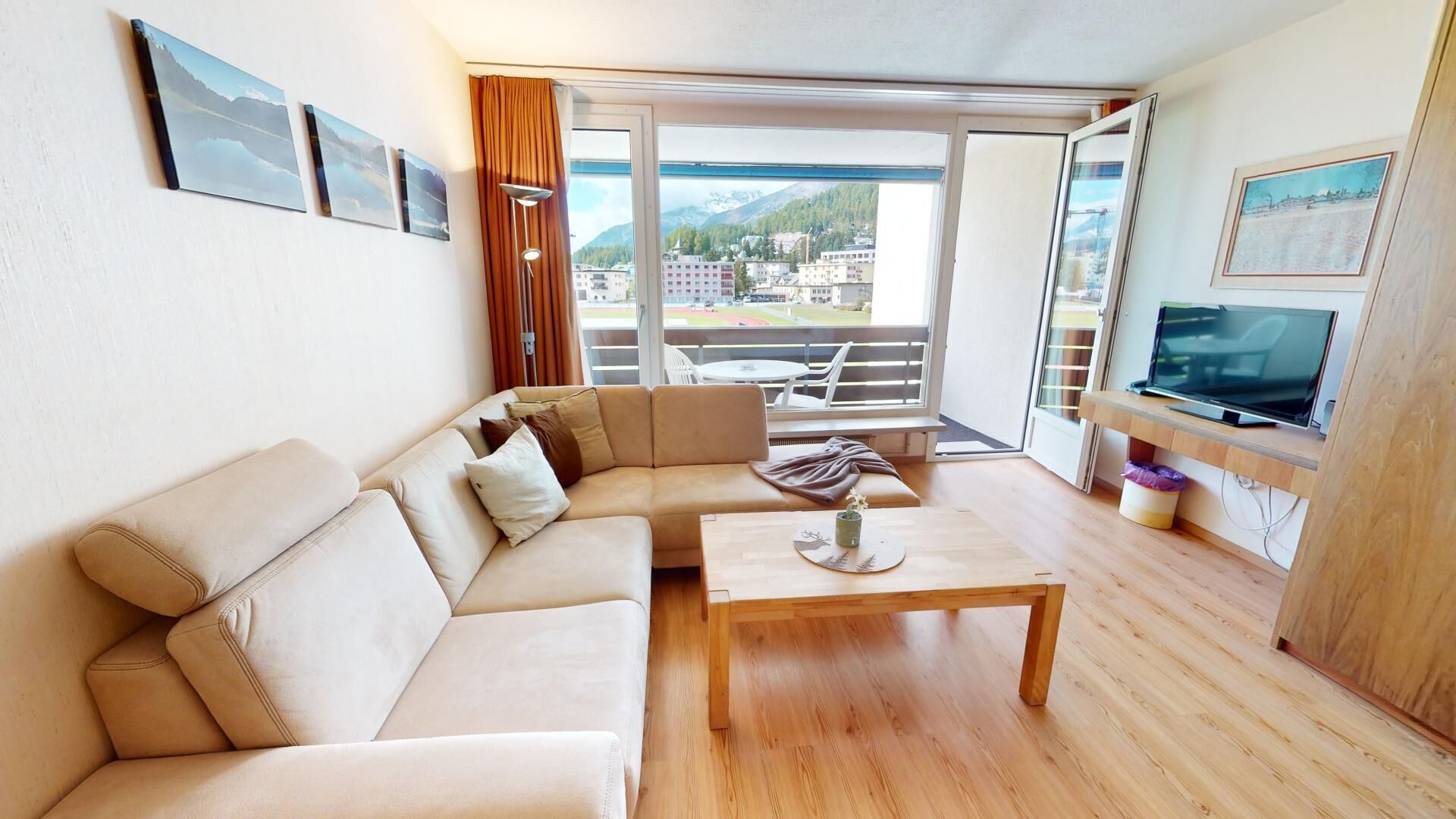 A modern living room with a beige sofa, a wooden coffee table, and a TV on a wooden stand.