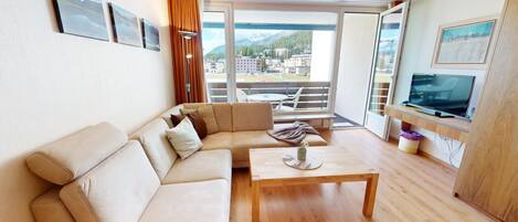 A modern living room with a beige sofa, a wooden coffee table, and a TV on a wooden stand.