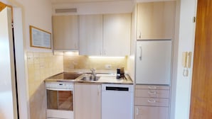 A compact kitchen with a dishwasher, a stove, a sink, and a refrigerator. There is a framed certificate on the wall and a telephone mounted on the wall. - Well-kept holiday apartament house in a prime location in St. (St. Moritz)