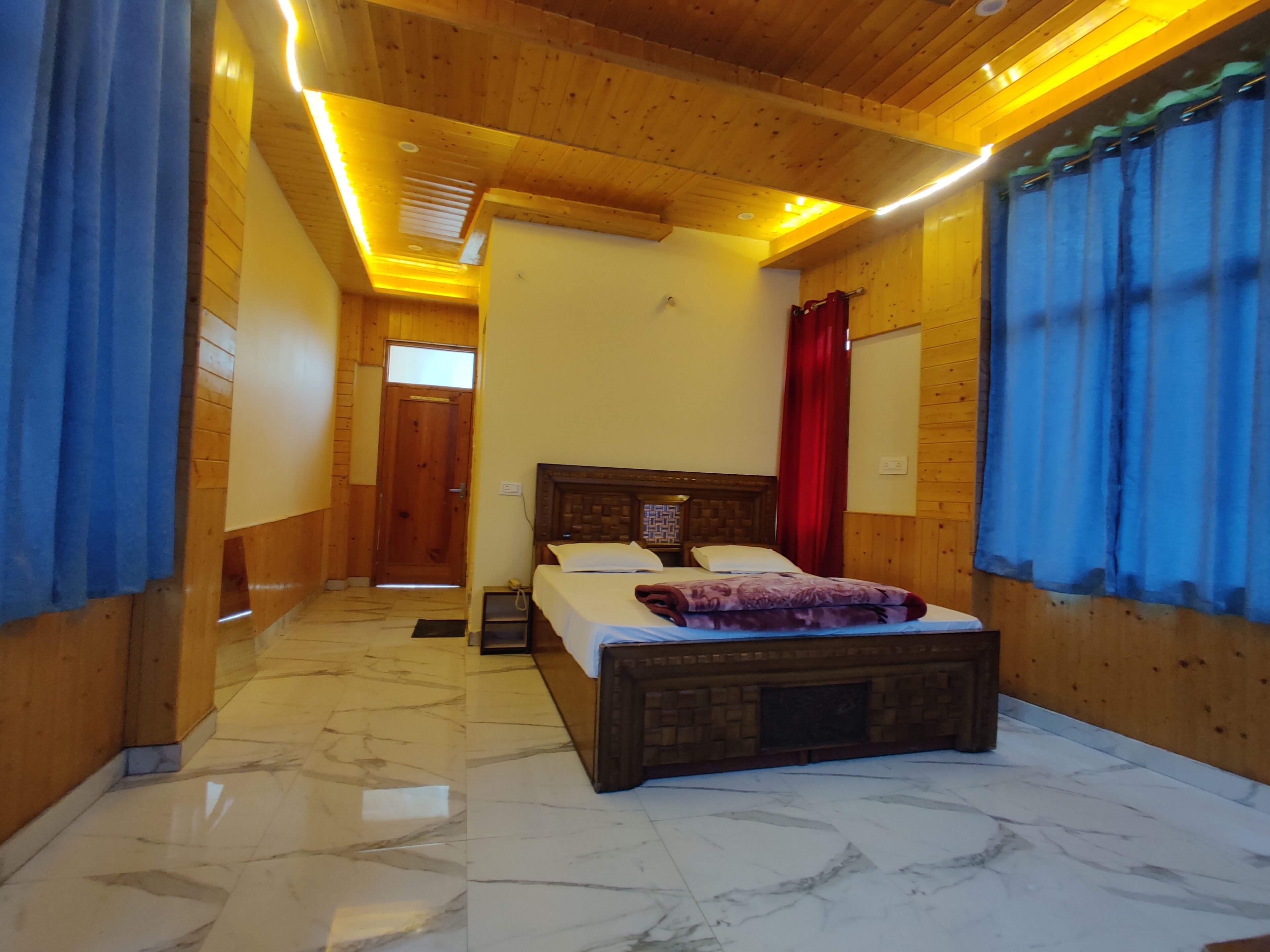 A bedroom with a wooden ceiling, a bed with a headboard, a nightstand, and a red curtain.