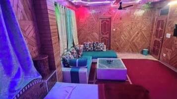 A room with a bed, a sofa, and a small table. There are wooden walls and a ceiling fan.