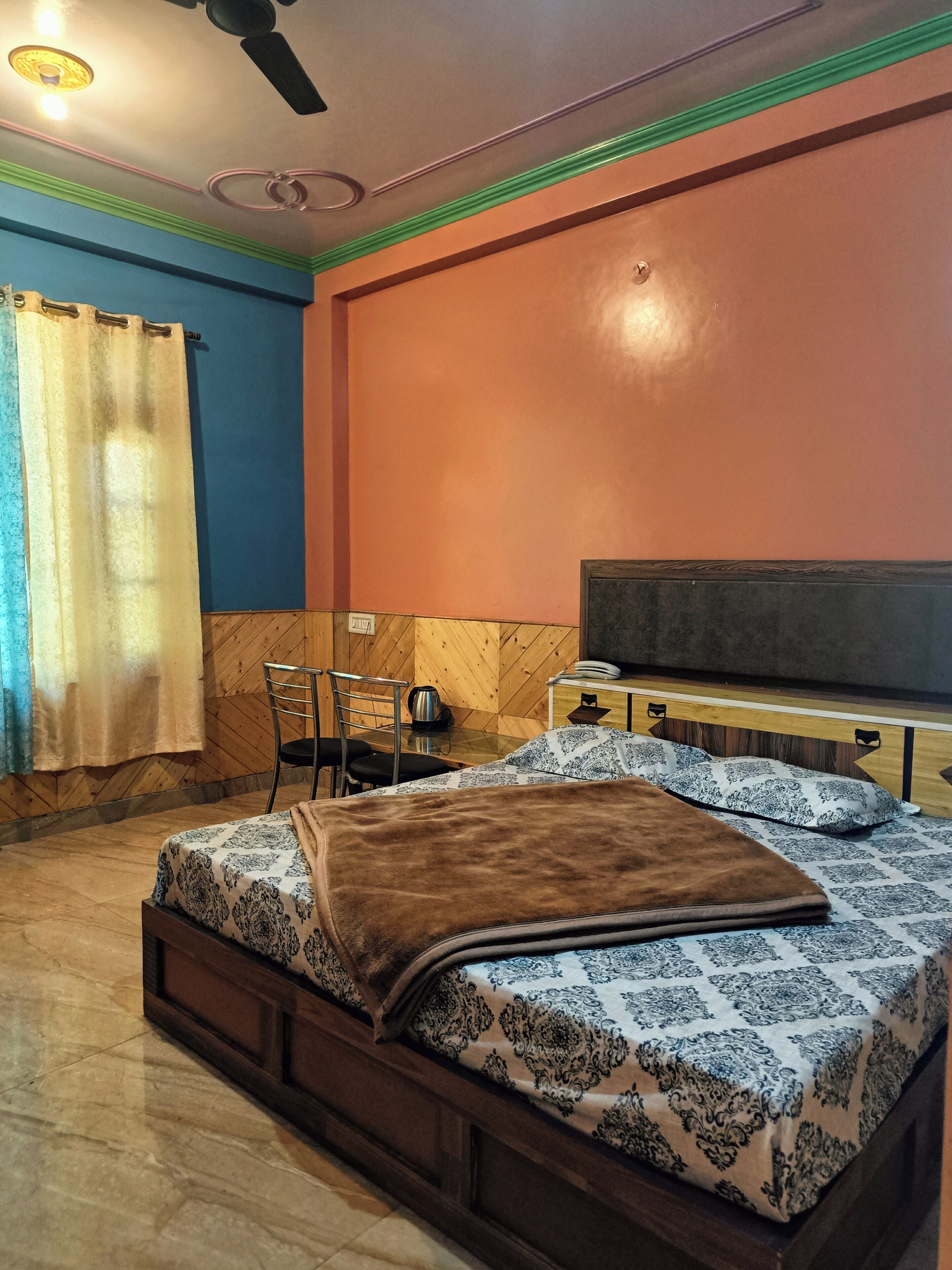Une chambre à coucher comprenant un lit, une chaise, une table, un téléviseur et une fenêtre avec des rideaux.