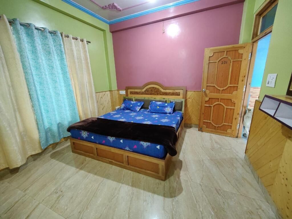 A bedroom with a wooden bed, a blue patterned bedspread, and a wooden wardrobe with a number '201' on it.