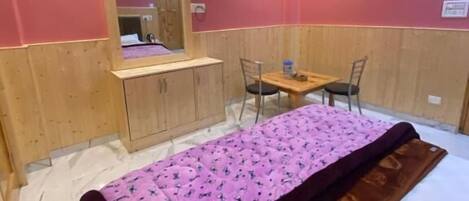A room with a bed, a wooden desk, a chair, and a mirror.