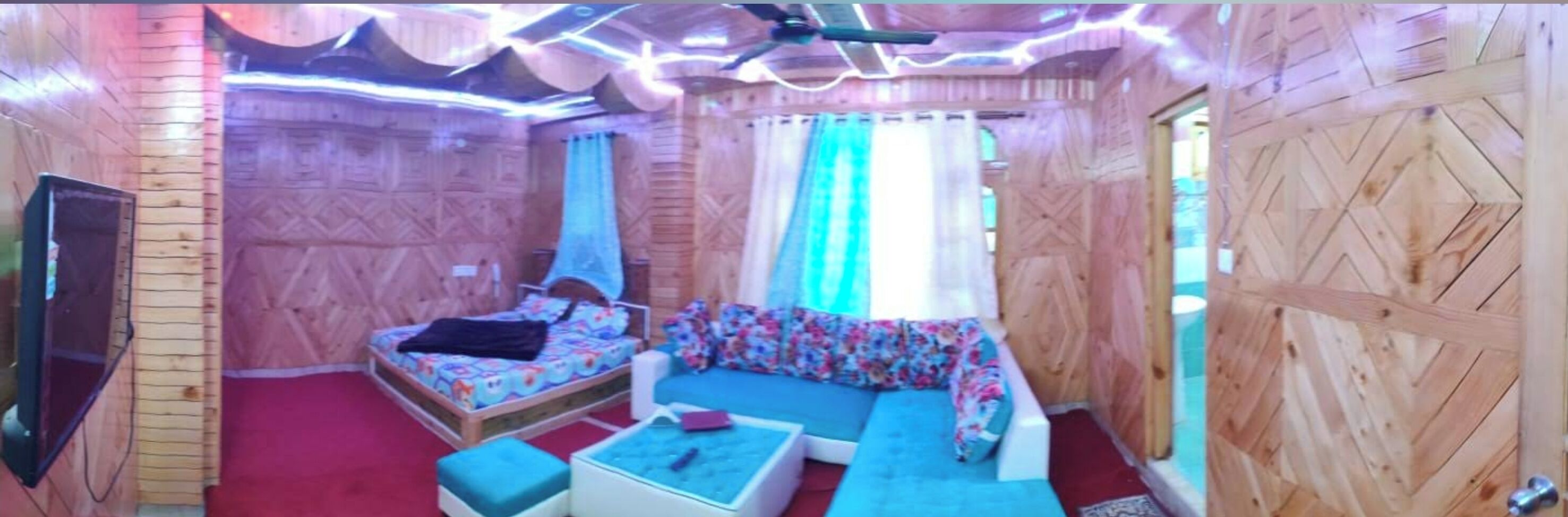 A room with wooden walls, a bed with floral bedding, a blue sofa, and a small table.