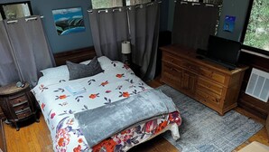Un dormitorio con cama, cómoda de madera, televisor y cortinas.