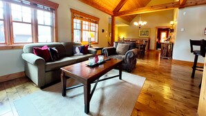 A spacious living room with a high wooden ceiling, a wooden dining table, and a cozy seating area with a sofa and armchairs. - Dreamcatcher Mountain Cabin - Ski-Bike-Golf-Relax (Kimberley)