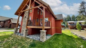 A large, red wooden house with a stone foundation, a balcony, and a stone wall base. - Dreamcatcher Mountain Cabin - Ski-Bike-Golf-Relax (Kimberley)