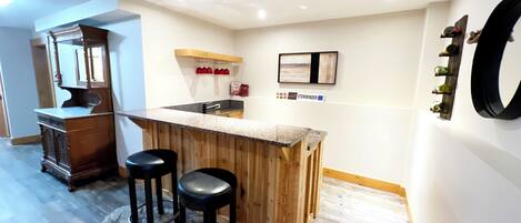 A compact kitchen with a wooden bar, two stools, and a refrigerator.