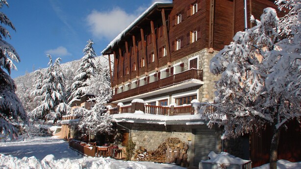 Un hotel de madera con balcones y fachada de piedra, rodeado de árboles cubiertos de nieve.