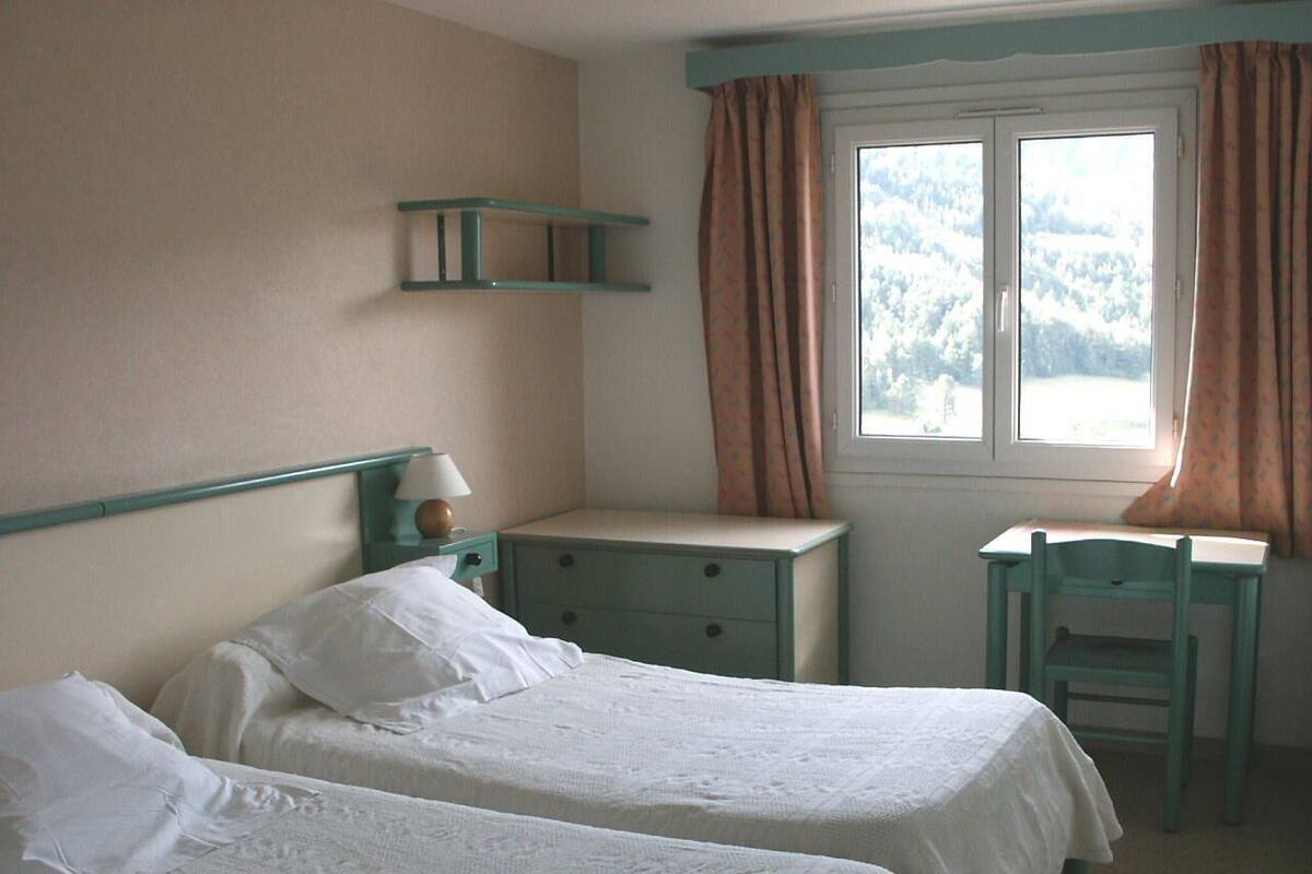 A bedroom with two single beds, a desk, and a chair.